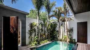 Una piscina al aire libre con cubierta de madera, rodeada de plantas tropicales y un edificio moderno con un amplio portal de madera.