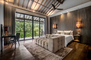 Un dormitorio moderno con una cama grande, una zona de estar, un escritorio y vistas a zonas verdes a través de grandes ventanales.