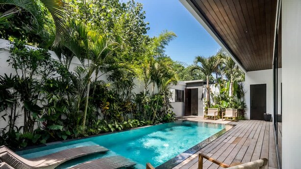 A swimming pool with lounge chairs, surrounded by lush greenery and a wooden deck. - Umayam Luxury Townhouse 7 (Pererenan)