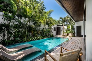 A swimming pool with lounge chairs, surrounded by lush greenery and a wooden deck. - Umayam Luxury Townhouse 7 (Pererenan)
