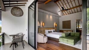 Ein modernes Hotelzimmer mit Bett, einem grünen Sofa, einem Esstisch mit Stühlen und Pendelleuchten.