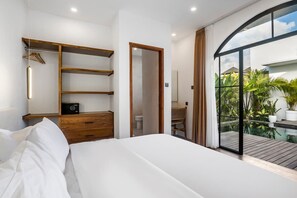 A modern bedroom with a large bed, wooden storage, a desk, and a balcony with plants. - Casa Copper in Kecamatan Mengwi (Kecamatan Mengwi)