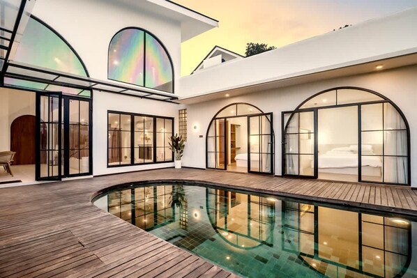 A modern house with a swimming pool, large arched windows, and a wooden deck. - Casa Copper in Kecamatan Mengwi (Kecamatan Mengwi)
