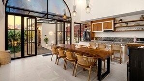 Uma cozinha moderna com uma ilha grande, armários de madeira e um espaço de jantar com uma mesa comprida e cadeiras de vime.