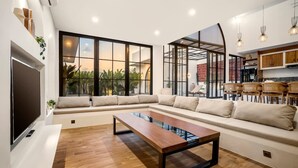 Uma sala de estar moderna com um sofá seccional, uma mesa de centro de madeira e uma grande janela com vista para o verde.