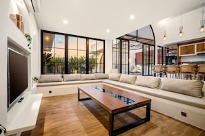 A modern living room with a sectional sofa, a wooden coffee table, and a large window with a view of greenery. - Casa Copper in Kecamatan Mengwi (Kecamatan Mengwi)