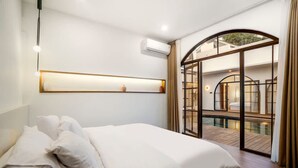 Quarto com uma cama grande, prateleira na parede, aparelho de ar condicionado e porta de vidro que dá para uma área de piscina.