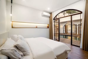 A bedroom with a large bed, a wall-mounted shelf, an air conditioning unit, and a glass door leading to a pool area. - Casa Copper in Kecamatan Mengwi (Kecamatan Mengwi)