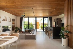 A spacious living area with a wooden ceiling, large windows, a sofa, a dining table, and a bar area. - Ben s Villa 2 in Kuta Utara (Kuta Utara)