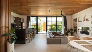 Un soggiorno moderno con soffitto in legno, ampie finestre, un divano, un tavolo da pranzo e un angolo cottura.