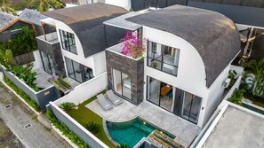 Ein modernes Haus mit gewölbtem Dach, einem Pool und einem Garten.