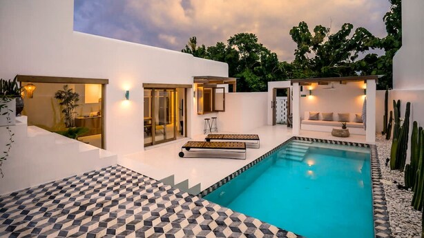 Un espace piscine moderne avec un motif géométrique en carreaux, une piscine et un mur extérieur blanc.