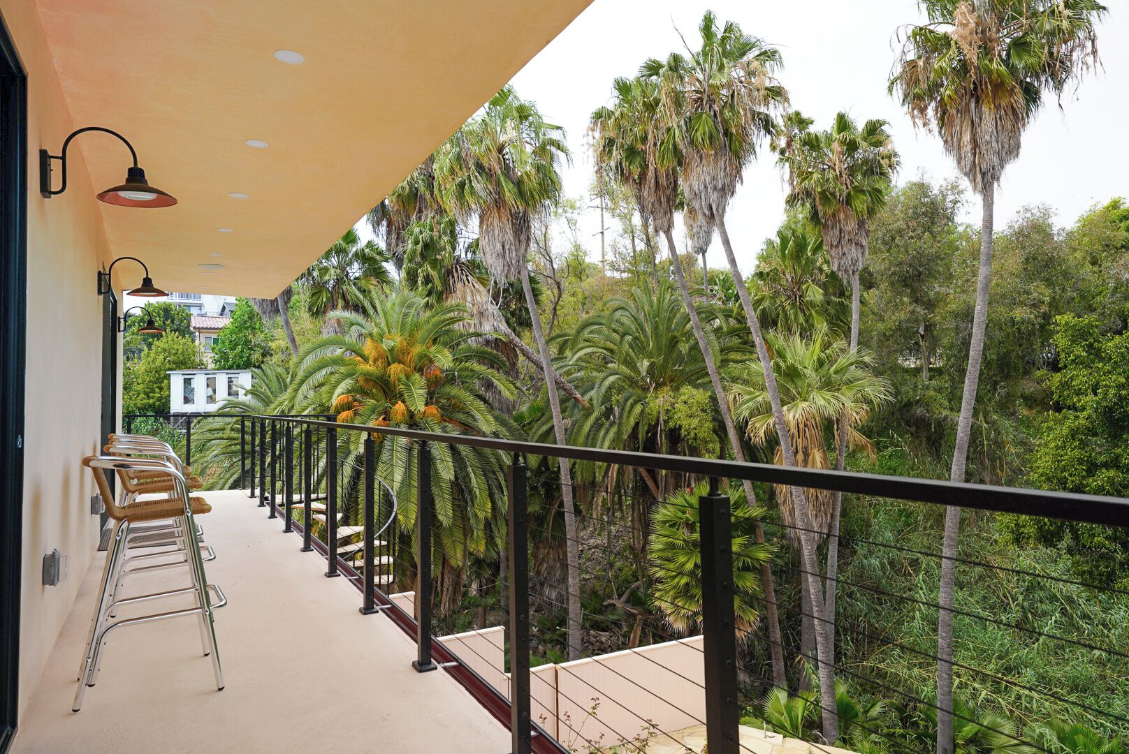 A balcony with a view of palm trees, a railing, and a chair.