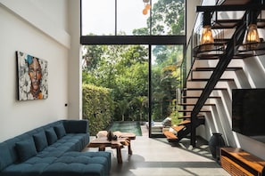 A modern interior with a sofa, wooden table, staircase, and a view of a lush garden. - Villa Kenji in Mengwi (Mengwi)