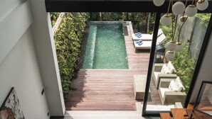 Un área de piscina moderna al aire libre con cubierta de madera, sillas de descanso y puerta de vidrio que da a la piscina.