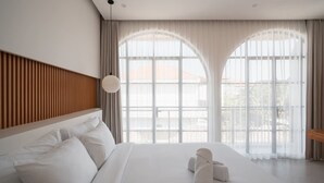 Hotellihuone, jossa on suuri sänky, kaksi ikkunaa, joissa on verhot, puinen pääty ja pyöreä valaisin.