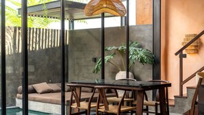 A modern interior with a glass table, wooden chairs, a hanging light fixture, a sofa, and a staircase. - The Mystik Loft Nirvana (Pererenan)
