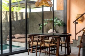 A modern interior with a glass table, wooden chairs, a hanging light fixture, a sofa, and a staircase. - The Mystik Loft Nirvana (Pererenan)