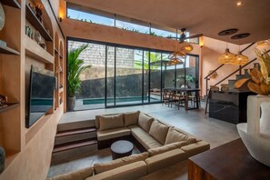 A modern living room with a sectional sofa, a flat-screen TV, a dining area with chairs, and a staircase leading to a balcony. - The Mystik Loft Nirvana (Pererenan)