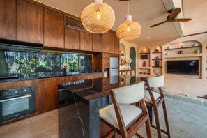 A modern kitchen with wooden cabinets, a large island, and pendant lighting. - The Mystik Loft Nirvana (Pererenan)