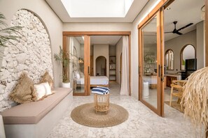 Ein modernes Interieur mit einer Steinwand, einem runden gewebten Hocker und einem Bett im Hintergrund.