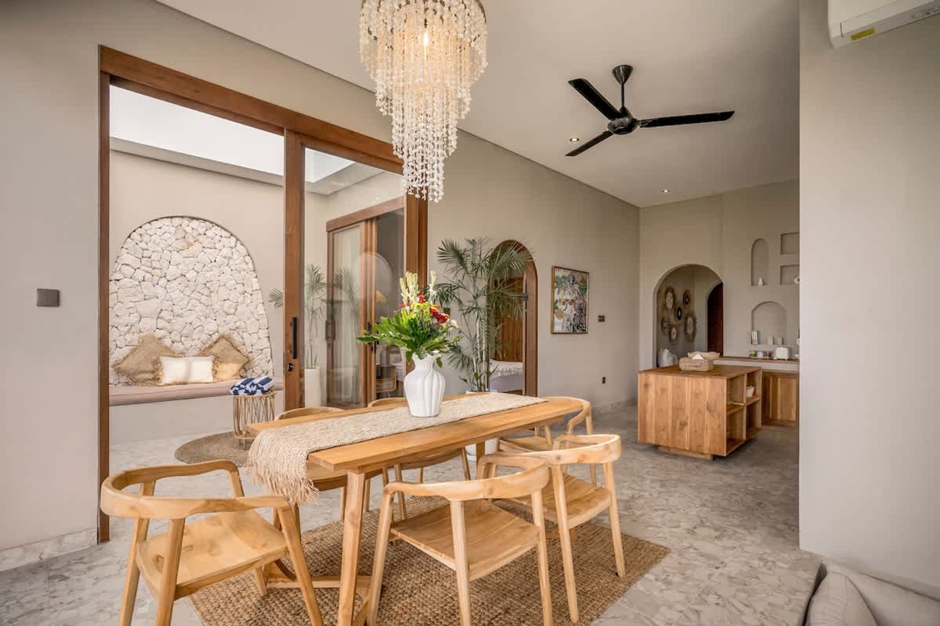 A dining area with a wooden table and chairs, a chandelier, and a ceiling fan.