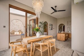 Ein Essbereich mit Holztisch und -stühlen, einer Kristallleuchtre und einem Deckenventilator.