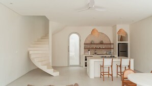 A modern kitchen with a central island, white cabinetry, and a spiral staircase leading to another level. - Villa Sari 1 in Bingin Beach (Bingin Beach)