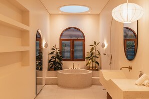 A modern bathroom with a freestanding bathtub, a vanity with a mirror, and two arched windows with blinds. - Villa Sari 1 in Bingin Beach (Bingin Beach)