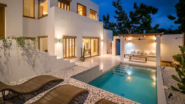 Ein modernes, zweistöckiges Haus mit Swimmingpool, Außenbereich zum Sitzen und einer gut beleuchteten Terrasse.