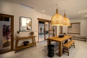 Un espace repas moderne avec une table en bois, des bancs et un grand luminaire suspendu en fibres tressées.