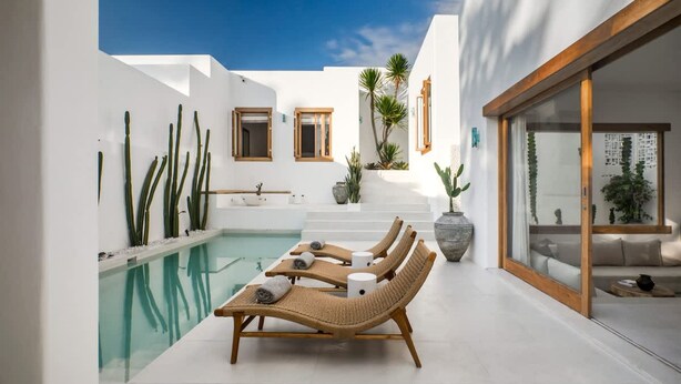Area piscina moderna all'aperto con lettini, cielo azzurro limpido e un edificio bianco con elementi in legno.