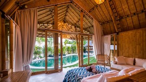 A room with a bed, a sofa, a table, and a view of a swimming pool. - 2BR Villa Bily in South Kuta (South Kuta)