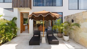 Eine moderne Lounge-Bereich im Freien mit zwei Liegestühlen, einem großen Sonnenschirm und Pflanzkübeln.