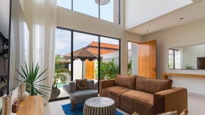 Ein stilvolles Wohnzimmer mit Sofa, Sessel, Couchtisch und Topfpflanzen.