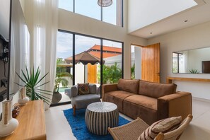 Ein stilvolles Wohnzimmer mit Sofa, Sessel, Couchtisch und Topfpflanzen.