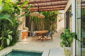A covered outdoor area with a pool, a dining table with chairs, and lush greenery. - Villa Rasa Rasa in Mengwi (Mengwi)