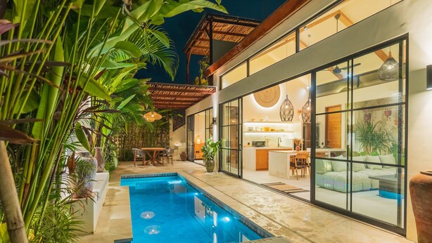 Une maison moderne dotée d’une piscine, de grandes fenêtres et de plantes tropicales.