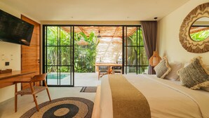Une chambre à coucher comprenant un lit, un bureau, une chaise, un téléviseur et donnant sur un jardin grâce à de grandes portes coulissantes.