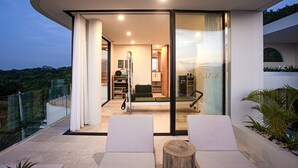 A modern interior with a glass door leading to a balcony, a seating area with cushions, and a visible exercise machine. - Villa Kalani Soul in South Kuta (South Kuta)