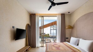 Ein Hotelzimmer mit einem Bett, einer Sitzbank, einem Fernseher, einem Deckenventilator und einem Balkon mit Blick.