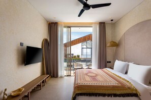 A hotel room with a bed, a bench, a TV, a ceiling fan, and a balcony with a view. - Villa Fresko 2 in Mengwi (Mengwi)