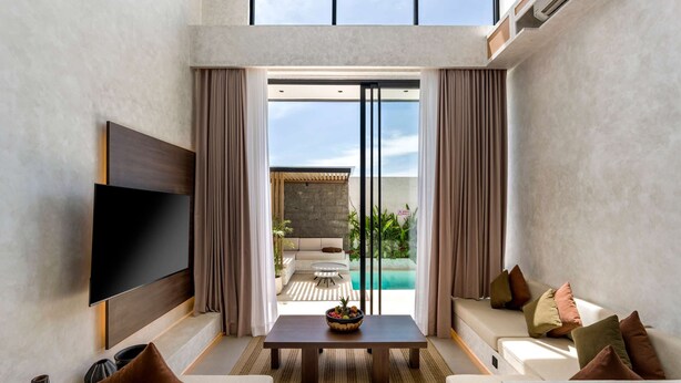 Un salon moderne doté d’un téléviseur à écran plat, d’un canapé, d’une table basse et offrant une vue sur un espace piscine extérieur.