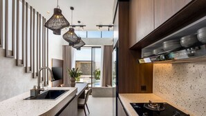 Une cuisine moderne dotée d’un comptoir incurvé, d’une cuisinière intégrée, de luminaires suspendus et donnant sur un balcon extérieur.