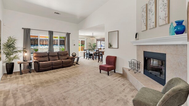A spacious living room with a fireplace, a sofa, and a dining area in the background.