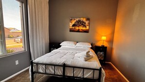 A bedroom with a bed, a nightstand, a lamp, a window, and a painting on the wall.