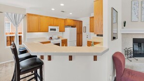 A modern kitchen with wooden cabinets, a white countertop, and a dining area with chairs.
