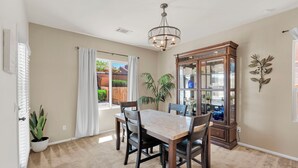 A dining room with a table and chairs, a chandelier, a cabinet with glass doors, and a potted plant.