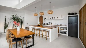 Una cocina moderna con una isla central, luces colgantes y un refrigerador.