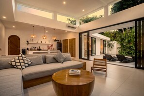 Ein modernes Wohnzimmer mit einer Couch, einem Couchtisch und einer Sitzecke mit Blick auf Grünflächen.